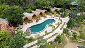 A resort with thatched-roof cottages, a central pool, and lush greenery. - The Goat Boutique Resort (Tay Hoa Lu)