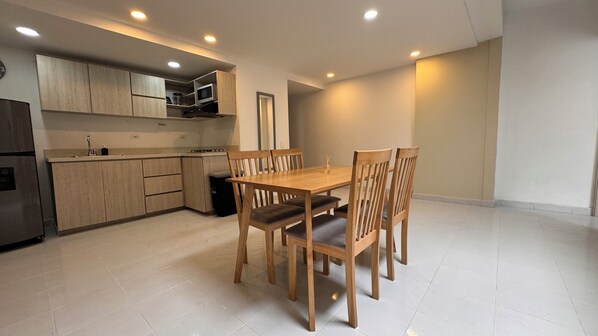 Een moderne keuken met houten kasten, een magnetron en een eethoek met een houten tafel en stoelen.