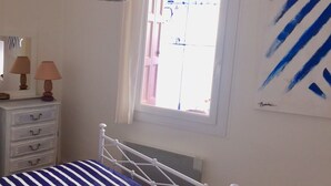 A bedroom with a bed, dresser, lamp, window, and artwork. - Maison Charmante au Cœur du Conflent (Sahorre)
