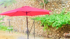 A picnic table with a red umbrella, set against a stone wall and surrounded by greenery. - Maison Charmante au Cœur du Conflent (Sahorre)