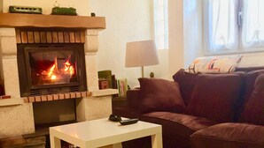 A living room with a fireplace, a sofa, a table, and a window. - Maison Charmante au Cœur du Conflent (Sahorre)