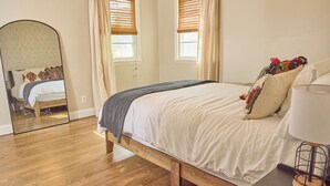 Een slaapkamer met een houten bed, witte beddengoed, een spiegel en een nachtkastje met een lamp.