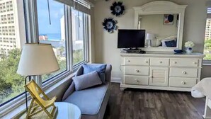 Ein Zimmer mit Sofa, Fernseher, Kommode und einem Fenster mit Stadtblick.