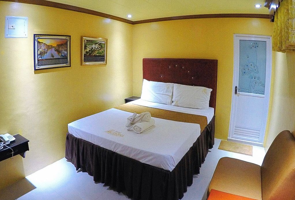 A hotel room with a bed, bedside table, and a door with a frosted glass panel.