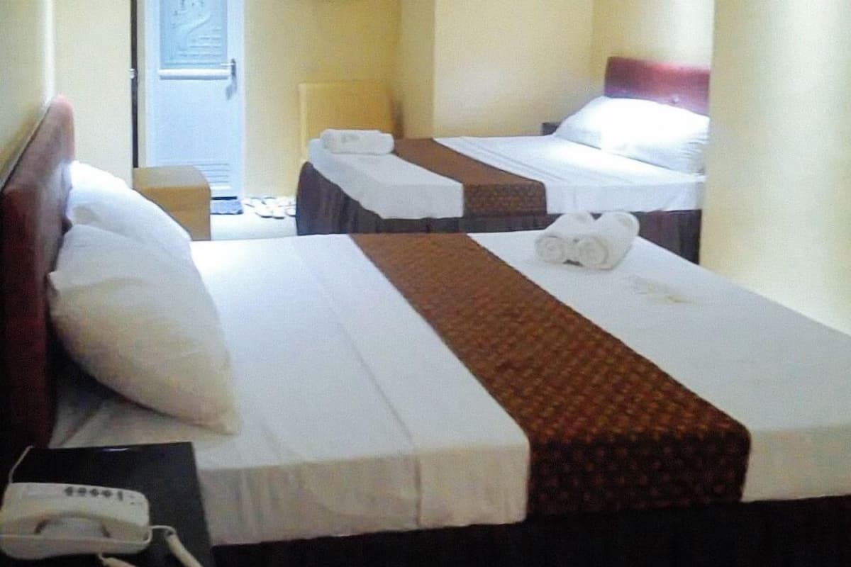 A hotel room with two beds, each with a white and brown bedspread, a bedside table with a phone, and a door leading to the hallway.