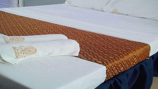 Un letto ben rifatto con una coperta a motivi e due asciugamani con un logo.