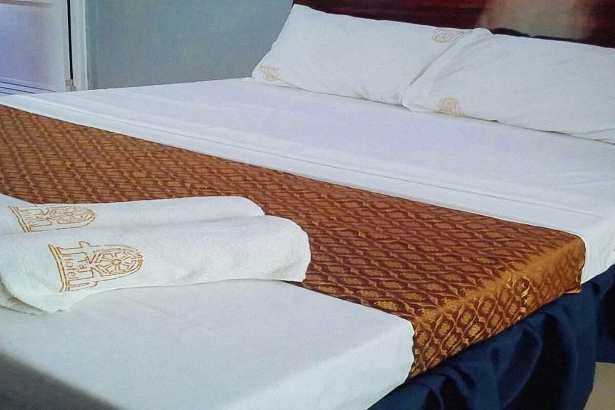 Un lit bien fait, avec une couvre-lit à motifs et deux serviettes ornées d’un logo.