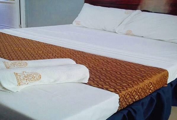 Un lit bien fait, avec une couvre-lit à motifs et deux serviettes ornées d’un logo.