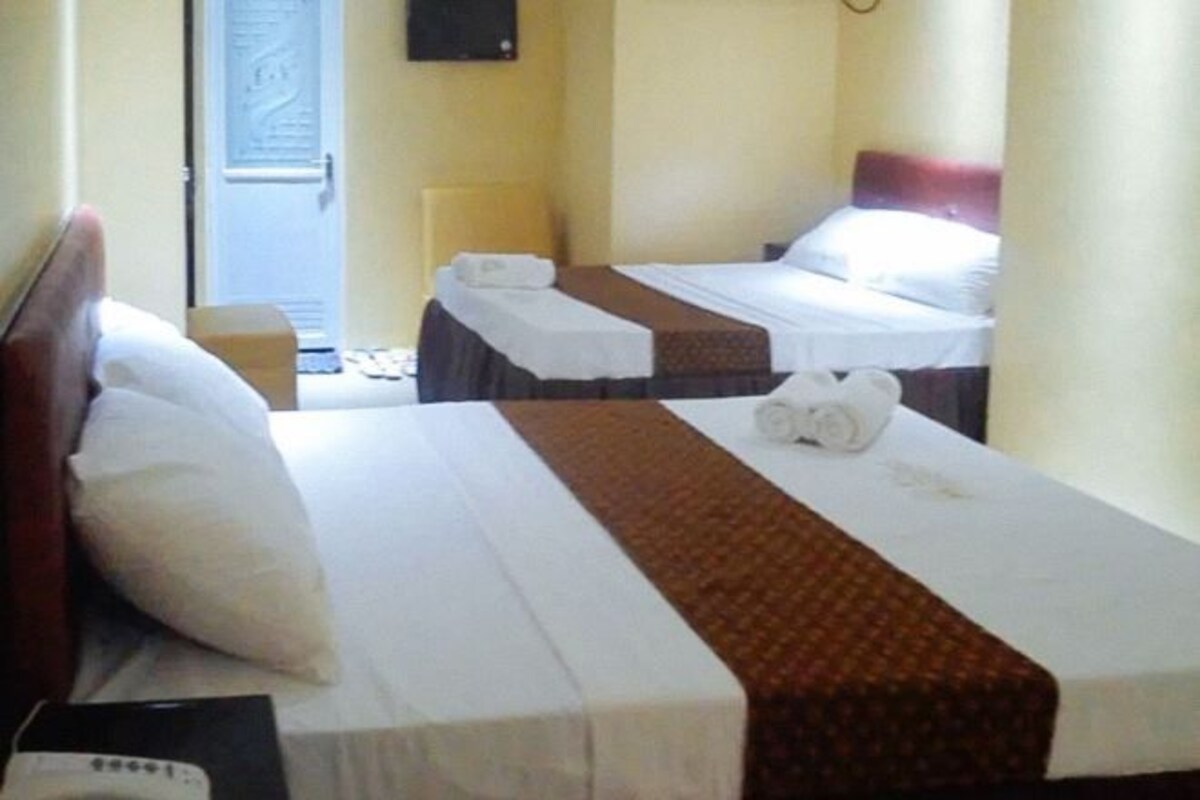 A hotel room with two single beds, a wooden headboard, a bedside table, and a small chair.