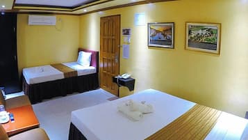 A hotel room with two single beds, a desk with a chair, a small table with a bottle and glasses, and a wall-mounted phone.
