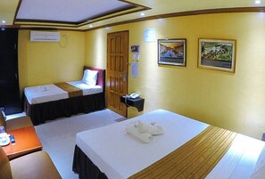 A hotel room with two single beds, a desk with a chair, a small table with a bottle and glasses, and a wall-mounted phone. - Reddoorz Plus @ Taj Hotel Tuguegarao (Tuguegarao)