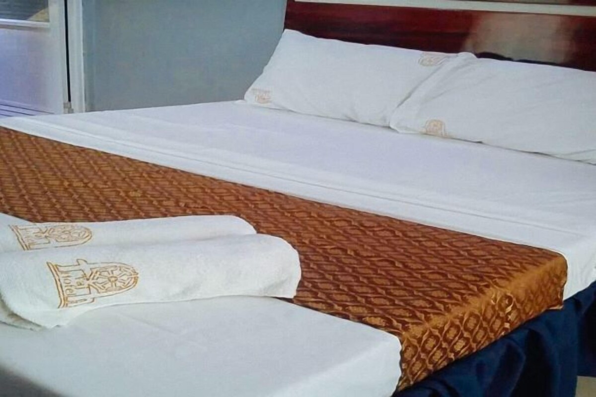 A hotel room with a bed, white bedding, a brown patterned bedspread, and a blue curtain.