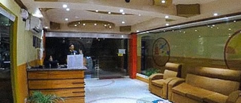 A lobby with a reception desk, a sofa, a coffee table, and a potted plant.