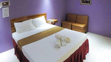 A hotel room with a bed, a nightstand, a brown leather chair, and a small table with a lamp.