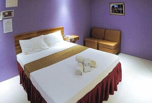 A hotel room with a bed, a nightstand, a brown leather chair, and a small table with a lamp. - Reddoorz Plus @ Taj Hotel Tuguegarao (Tuguegarao)