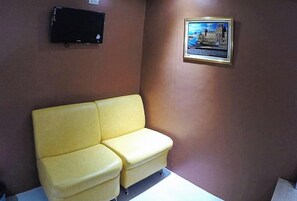 Un sofá amarillo en una habitación con pared marrón, un cuadro enmarcado y un televisor de pantalla plana.