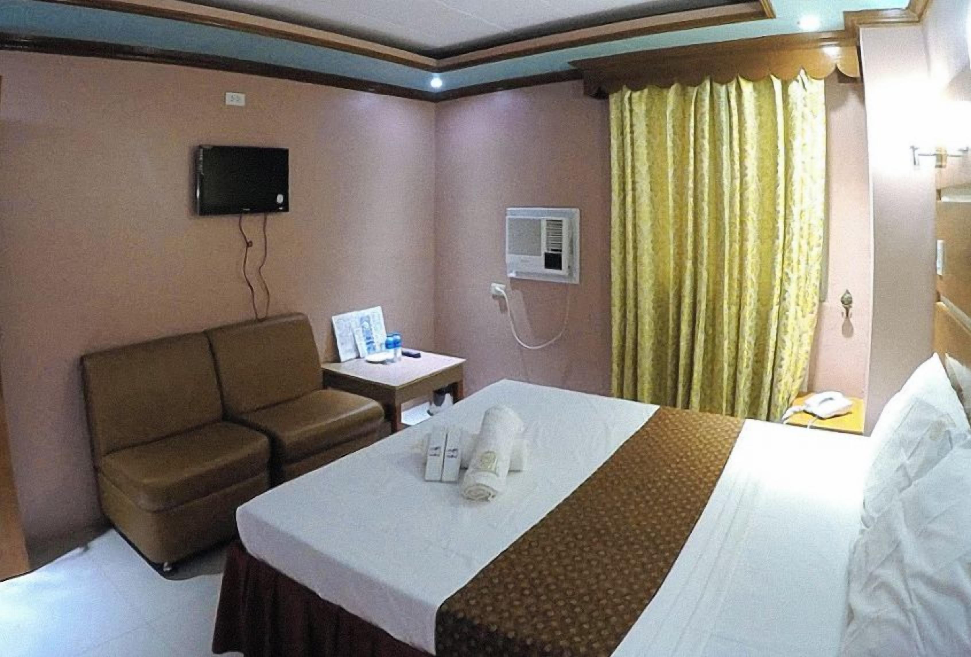 Hotelkamer met een bed, een slaapbank, een klein tafeltje met een televisie, een airconditioningsysteem en een gordijn.