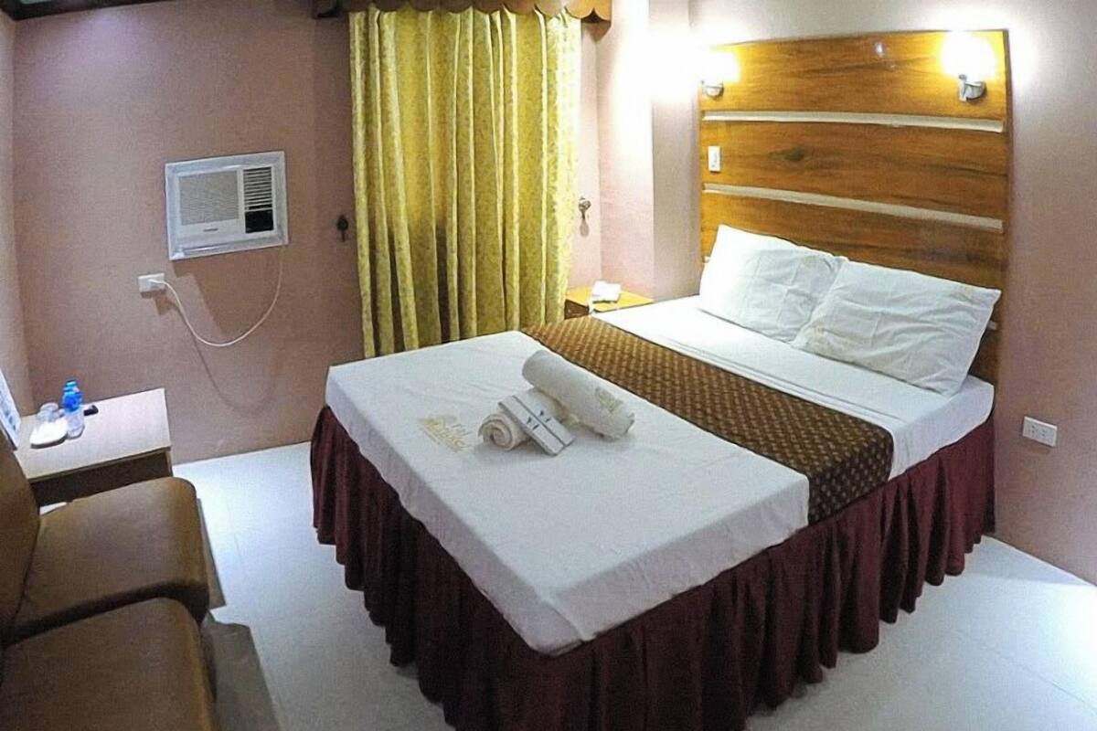A hotel room with a bed, a desk, a chair, a nightstand, a lamp, and a window with curtains.