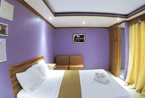 A hotel room with a bed, a sofa, a small table, and a window with curtains. - Reddoorz Plus @ Taj Hotel Tuguegarao (Tuguegarao)