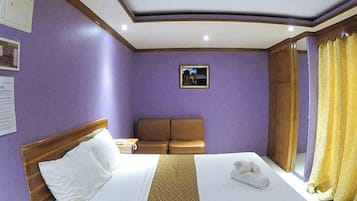 A hotel room with a bed, a brown sofa, a small table, and a window with curtains.
