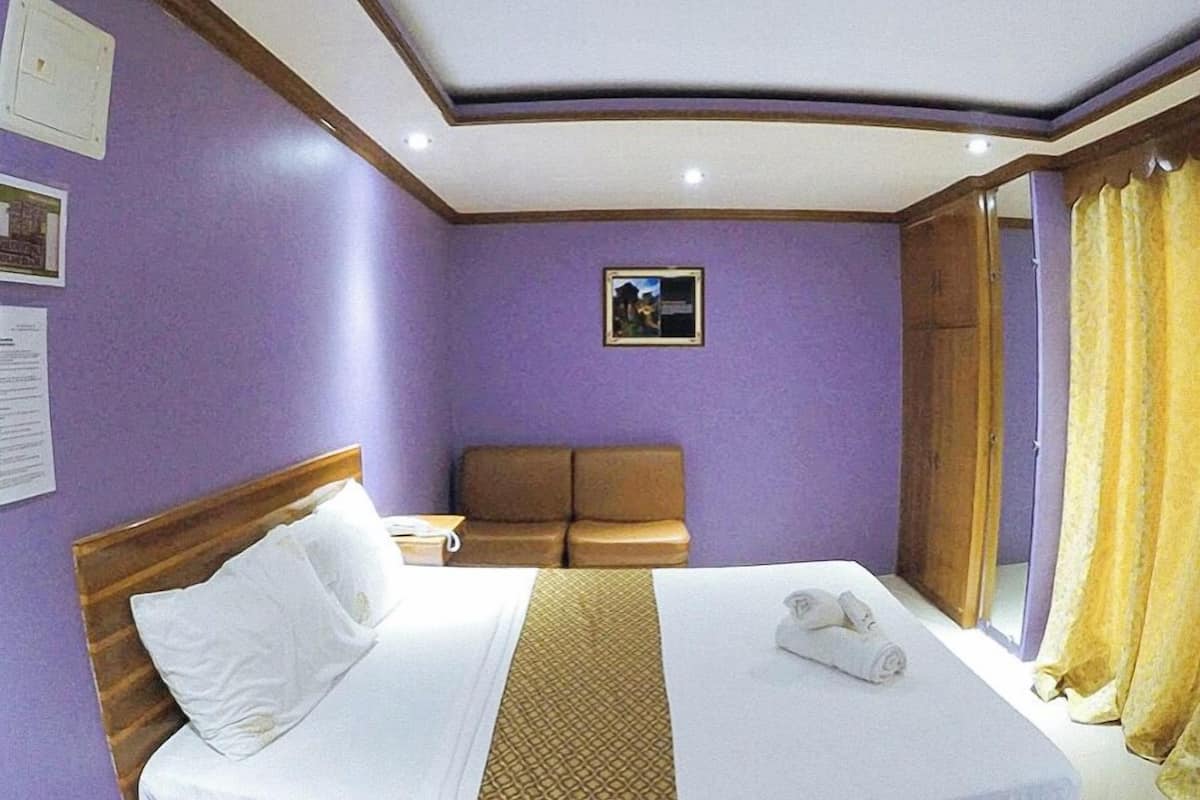 A hotel room with a bed, a sofa, a small table, and a window with curtains.