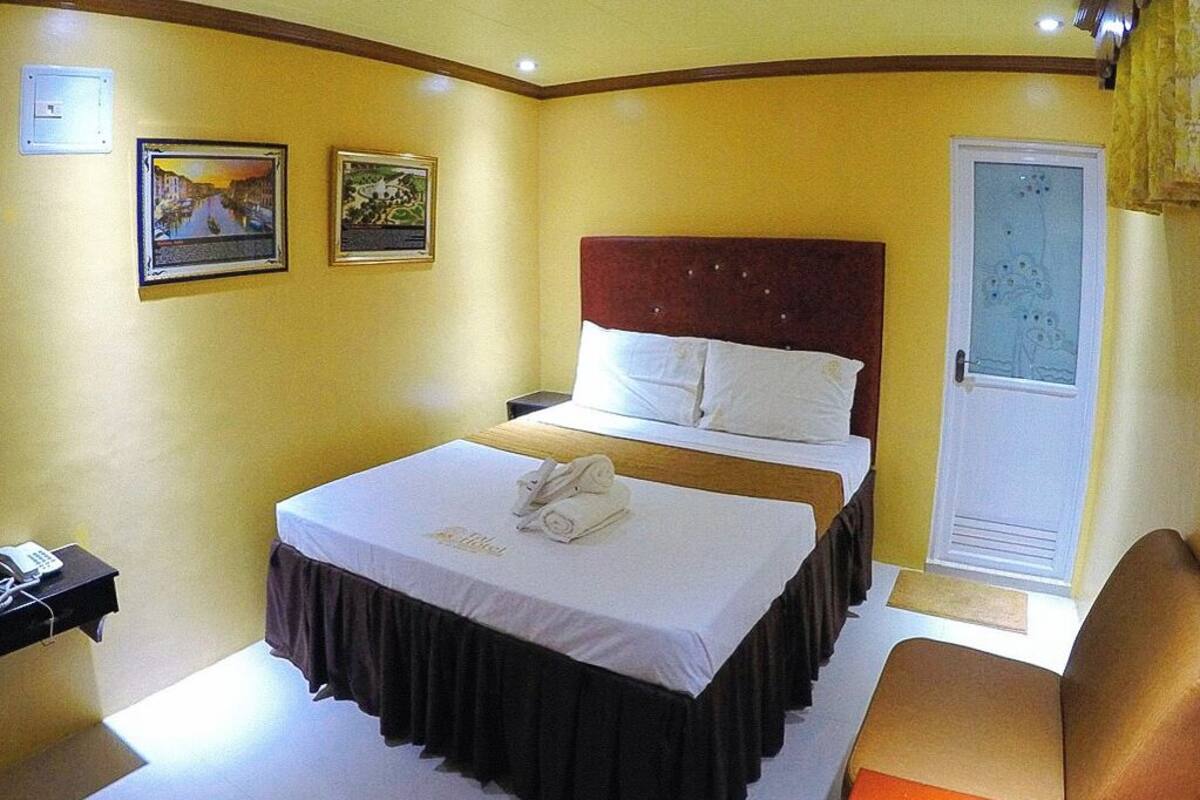 A hotel room with a bed, bedside table, and a door with a frosted glass panel.