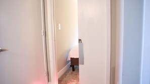 Enter a cozy room with a door on the left and a bed or table at the end of the hallway.