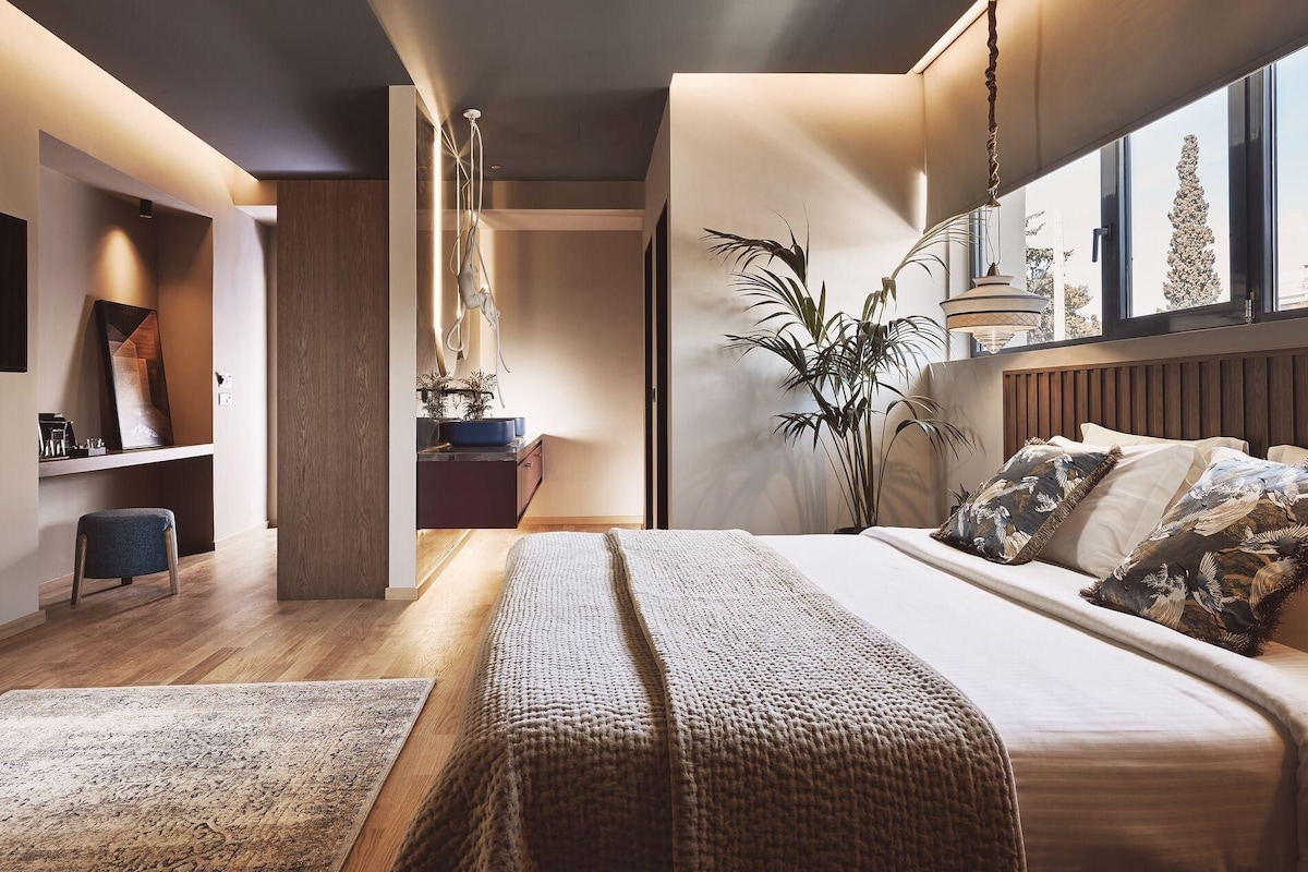 A modern bedroom with a large bed, a desk, a chair, and a plant.