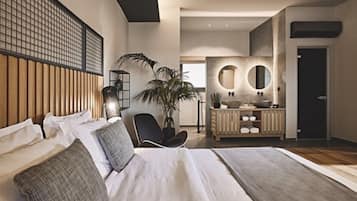 A modern bedroom with a large bed, a bedside table, a chair, and a bathroom with a vanity and mirrors.