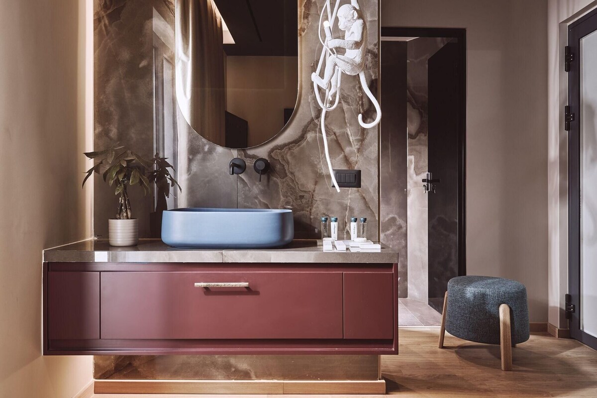 Un bagno moderno con parete in marmo, lavandino blu e una panca in legno.