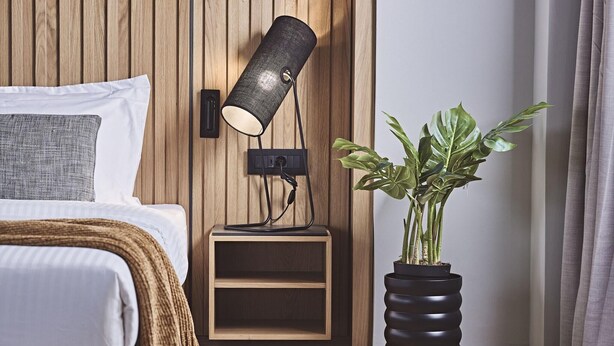 A bedroom with a bed, bedside table, lamp, and potted plant.
