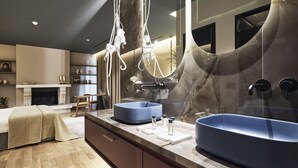 A modern bathroom with two large blue sinks, a marble wall, and a large mirror.