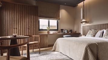 A cozy bedroom with a large bed, a wooden wardrobe, a small table with chairs, and a window with a view.