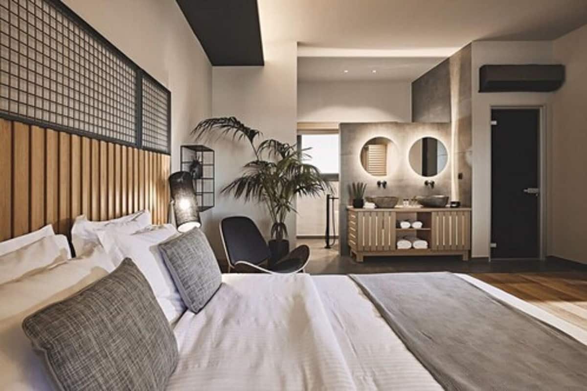 Ein modernes Schlafzimmer mit einem großen Bett, einem Schreibtisch und einem Badezimmer mit einem runden Spiegel.