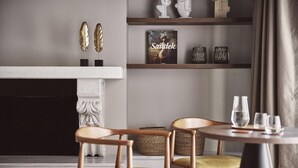 A modern living room with a fireplace, wooden chairs, a round table with glasses, and decorative items on shelves.