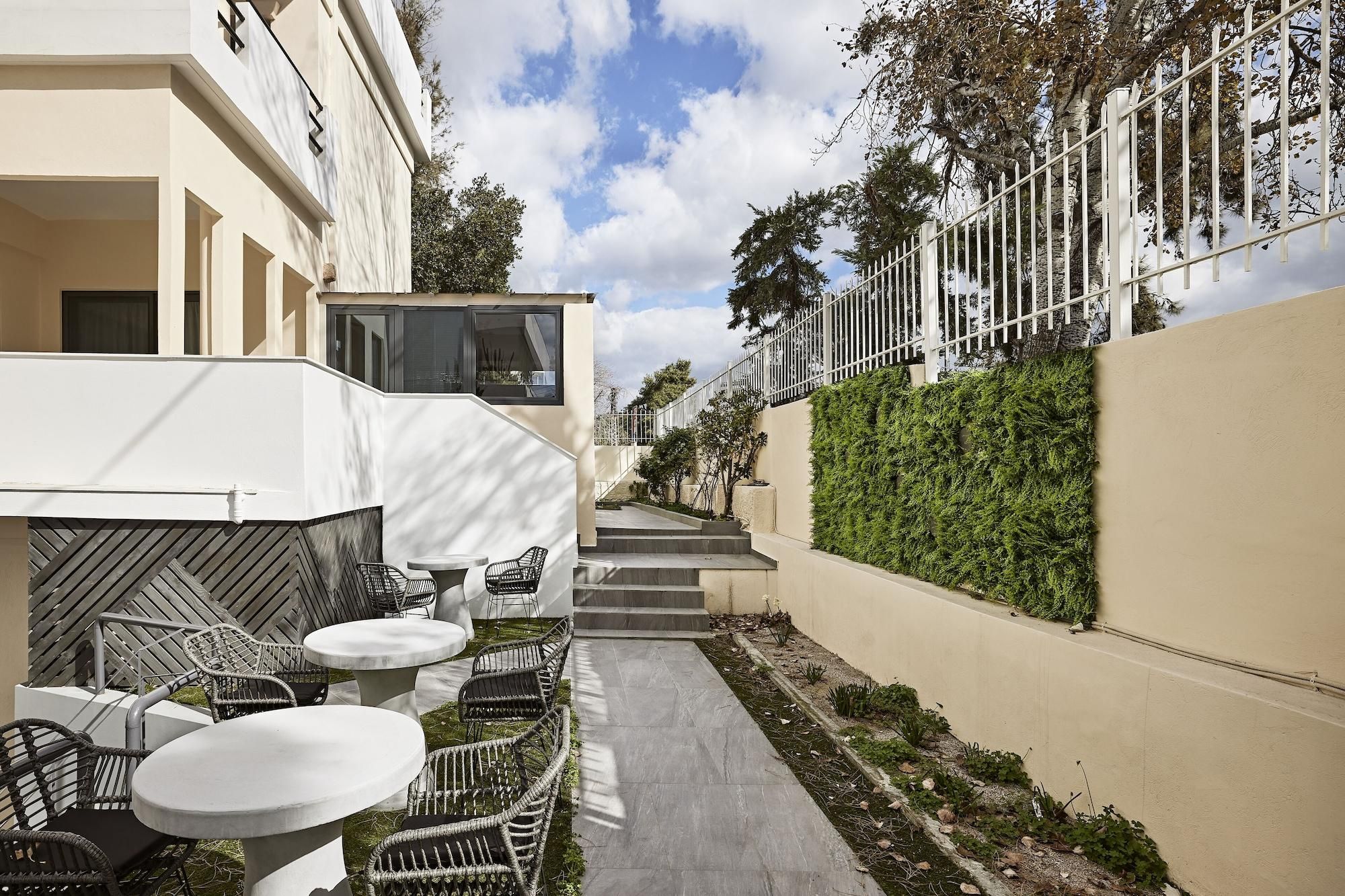 A narrow outdoor corridor with steps leading to a building entrance, surrounded by greenery and a white fence.