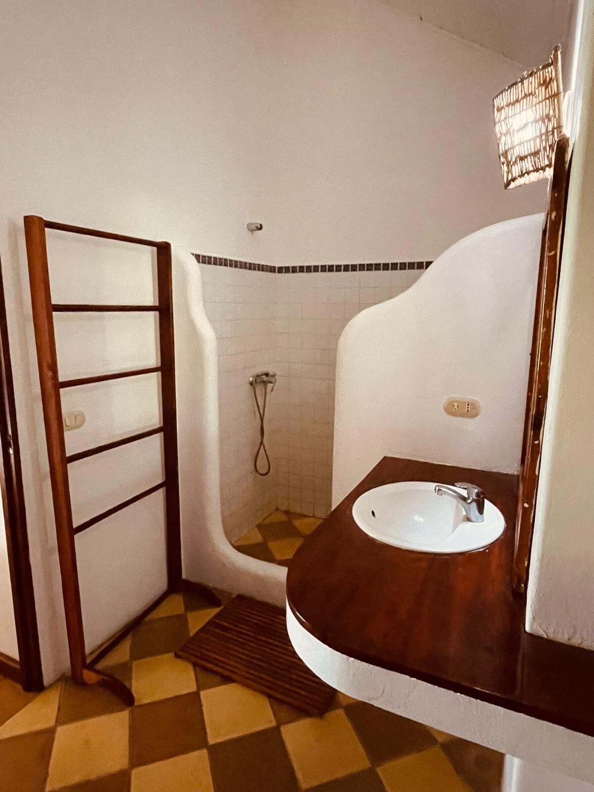 Un baño con tocador de madera, un lavamanos blanco, un espejo y una ducha con pared de azulejos.