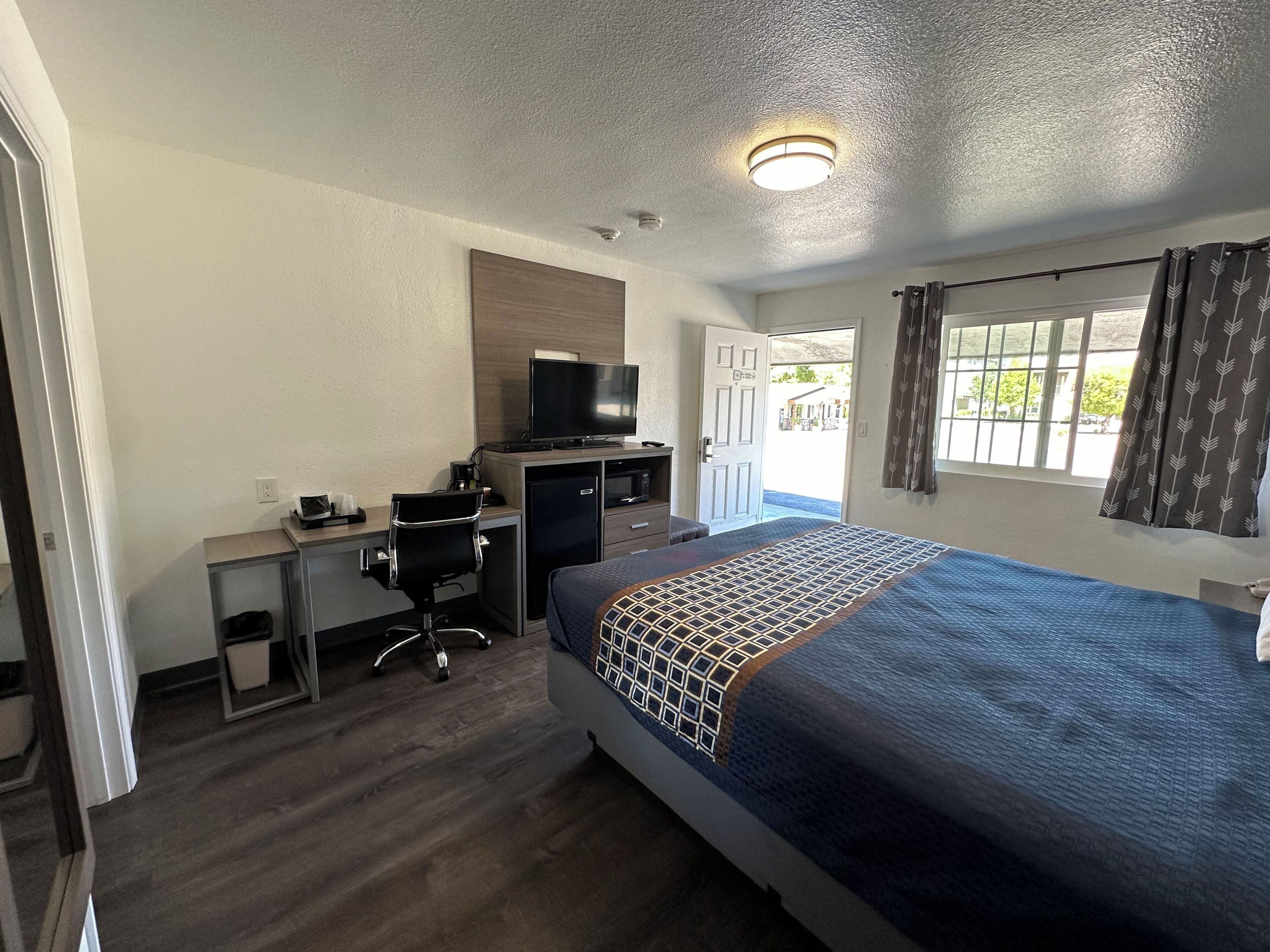 A hotel room with a bed, desk, chair, television, and a window with curtains.