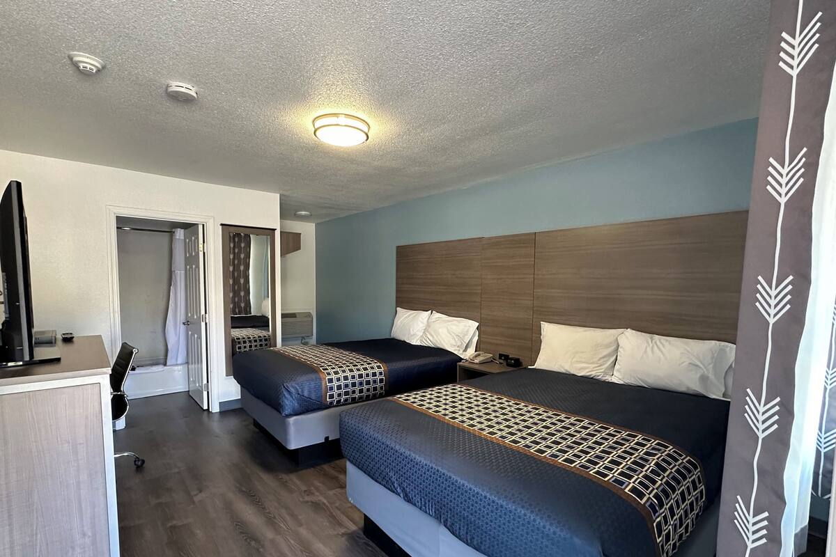 A hotel room with two beds, a desk, and a shower area.