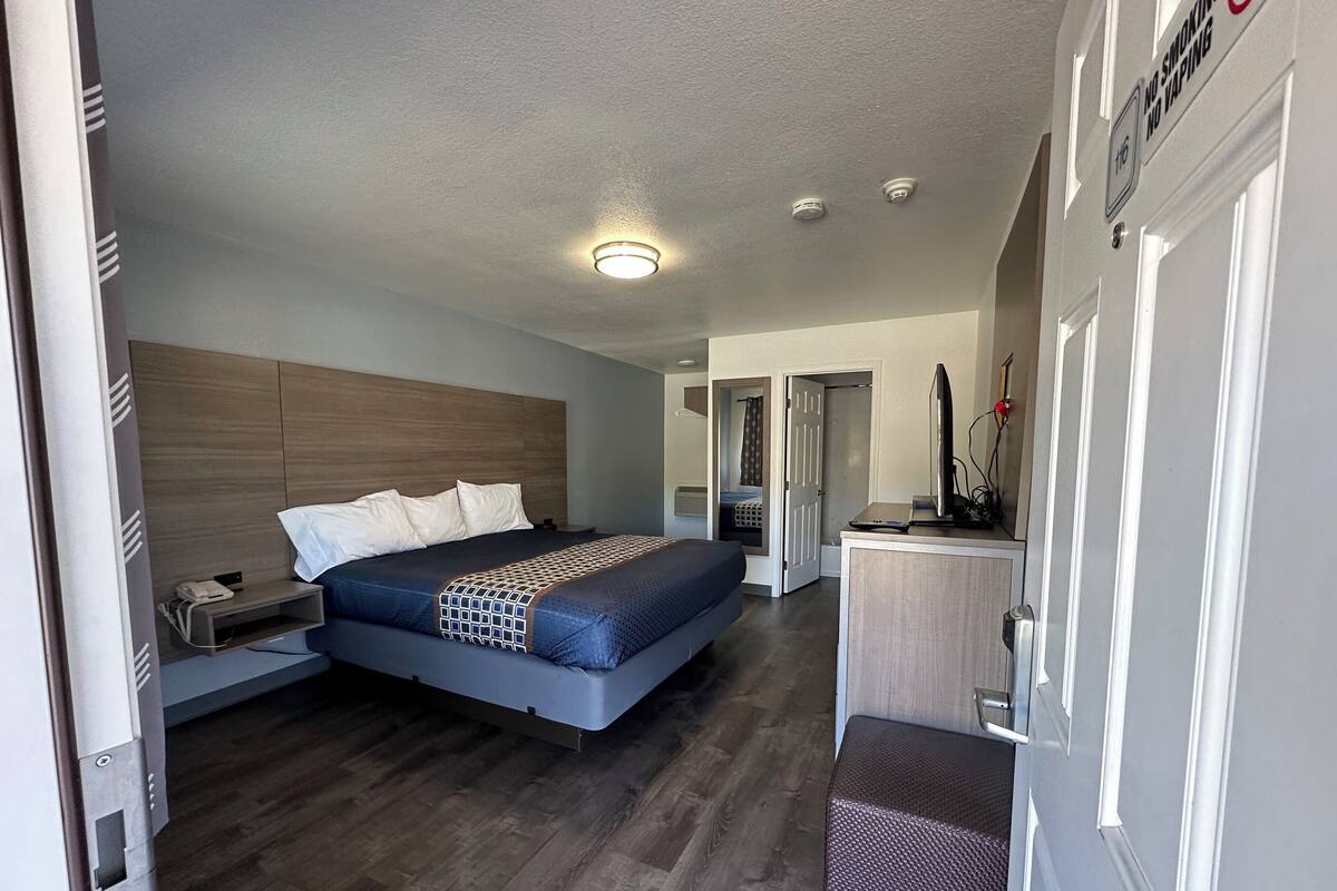 A modern hotel room with a large bed, bedside tables, a desk with a computer, and a small seating area.