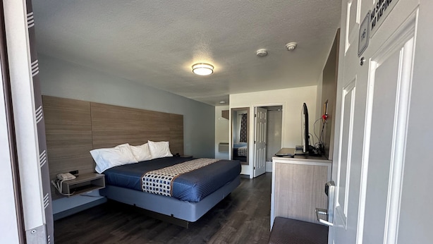 A modern hotel room with a large bed, bedside tables, a desk with a computer, and a small seating area. - Sands Motel (Livermore)