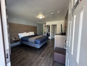 Una habitación de hotel moderna con una cama grande, mesitas de noche, un escritorio con ordenador y una pequeña zona de estar.