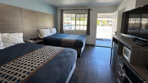 A hotel room with two beds, a TV, a desk, and a window with a view of the street. - Sands Motel (Livermore)