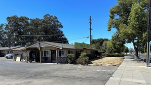 A small motel with a single-story structure, a covered parking area, and a sidewalk adjacent to the building. - Sands Motel (Livermore)