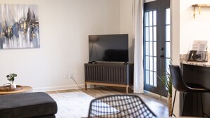 A modern living room with a flat-screen TV, a dark-toned entertainment unit, a grey sofa, a patterned chair, and a small side table with a plant. - Golf Course Views, Sunsets & Chill Vibes (Lowndes County)