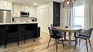 A modern kitchen with white cabinets, a central island with bar stools, a dining table with chairs, and pendant lighting. - Golf Course Views, Sunsets & Chill Vibes (Lowndes County)