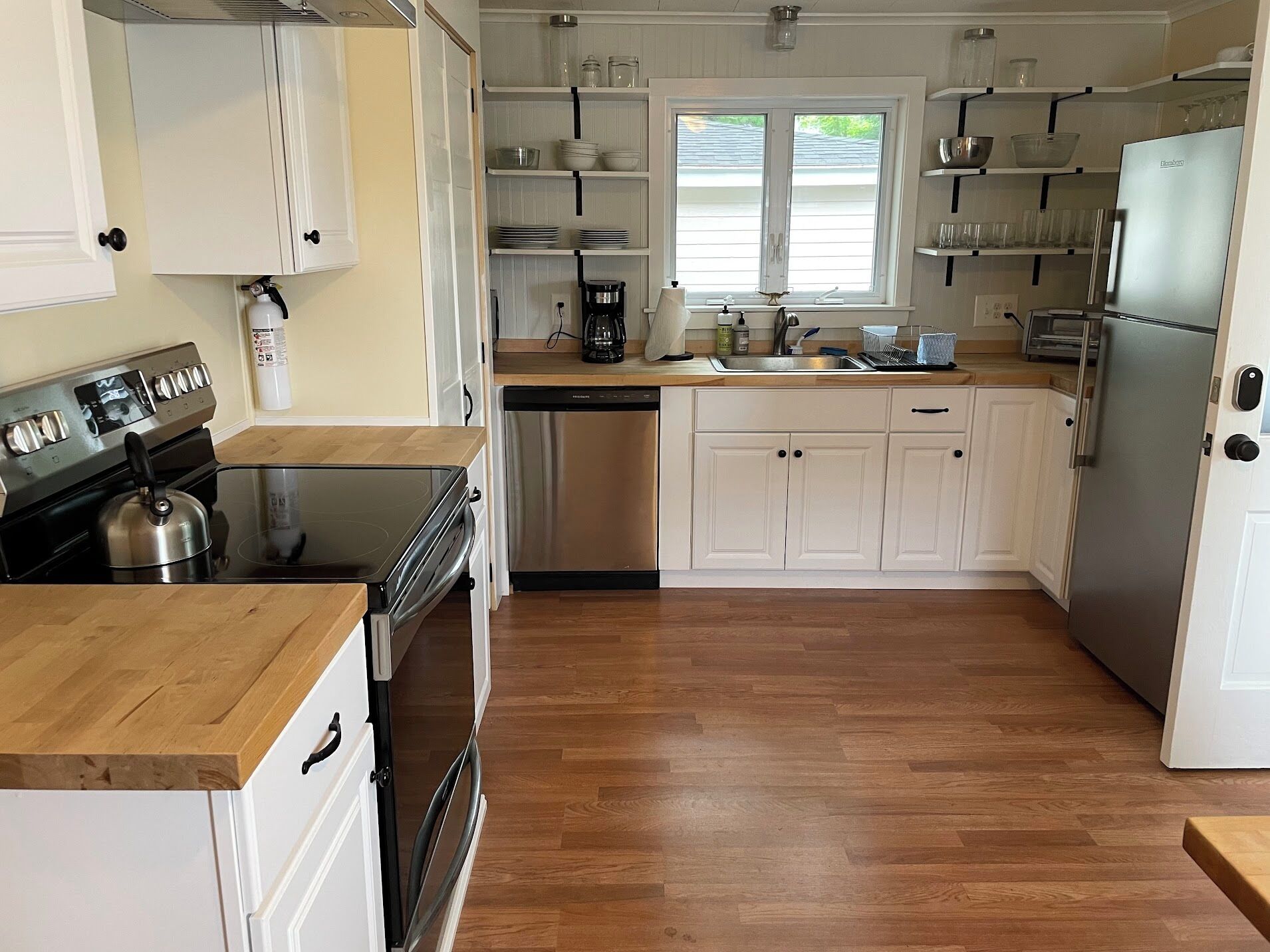 A modern kitchen with white cabinets, a stainless steel refrigerator, a dishwasher, and a coffee maker.
