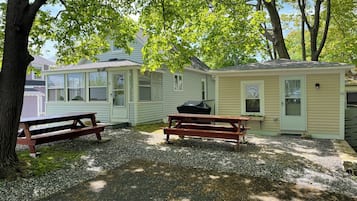 A small, single-story cabin with a porch and two picnic tables.