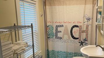 A bathroom with a shower curtain featuring a beach theme, a toilet, a sink, and a metal shelf unit with towels.