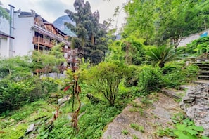 A lush garden with a variety of plants and trees, a stone pathway, and a building with balconies. - Yangshuo wanglai Hotels (Yangshuo)